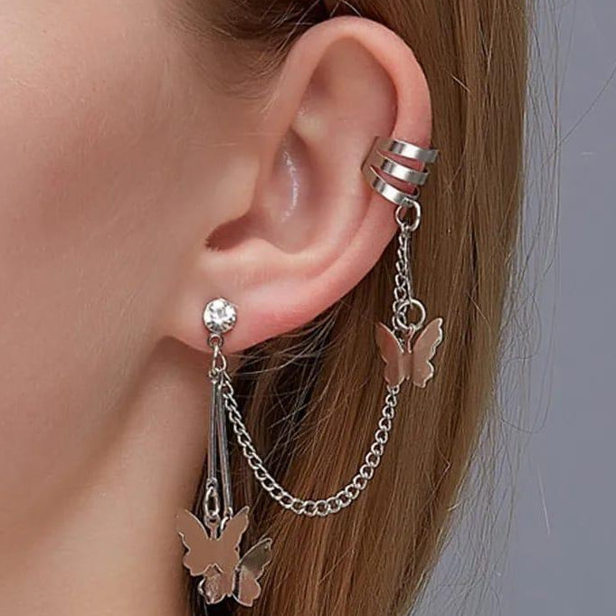 Silver butterfly earring with chain detail worn on an ear against a neutral background